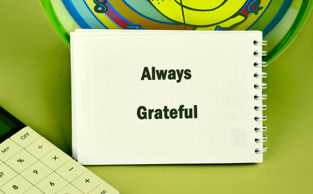 A notepad opened to reveal the words always grateful rests next to a calculator, with a vibrant clock in the background, showcasing an uplifting atmosphere focused on appreciation.の写真素材