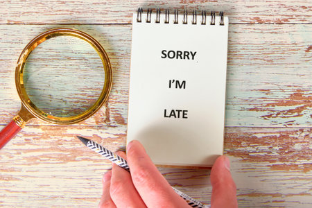 A hand holds a notebook open showing the text Sorry Im Late next to a magnifying glass and a...
