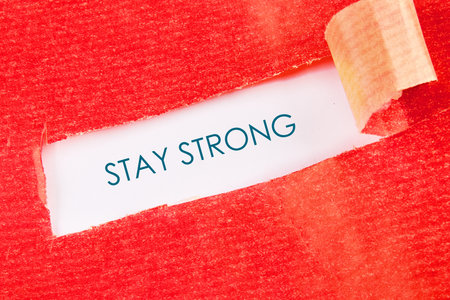 A red surface is torn to reveal a message of encouragement. The words STAY STRONG are written in teal blue underneath the opening. A beige adhesive tape is used to stick the torn surface.の写真素材