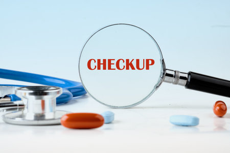 A stethoscope and different kinds of medicine lay on a white table, with a magnifying glass hovering over the word Checkup, referring to medical healthcare and health evaluation.の写真素材