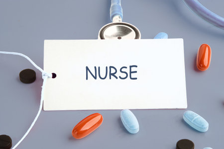 Display shows a stethoscope draped over a sign with the word Nurse. Medicine pills in orange, blue, and dark colors scatter on a gray background.の写真素材