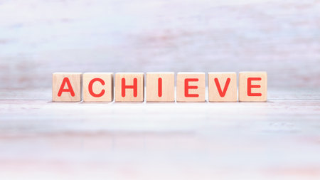 The word achieve is spelled out using red letters on wooden toy blocks. It suggests achievement, setting goals, and working towards success.の写真素材