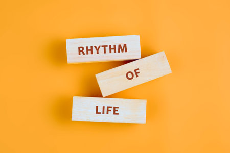 Wooden blocks, neatly stacked, spell out the phrase RHYTHM OF LIFE. The arrangement is simple yet meaningful, set against a plain orange backdrop.の写真素材
