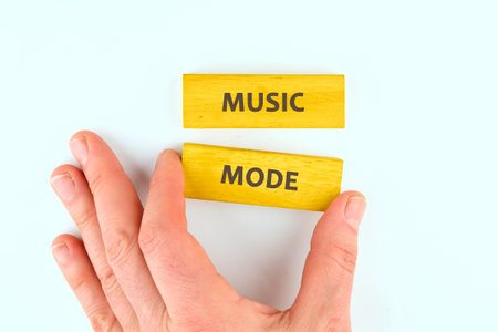 A hand carefully places a wooden block reading MODE beneath another block that reads MUSIC. This illustrates the activation of creative sound and musical exploration.の写真素材