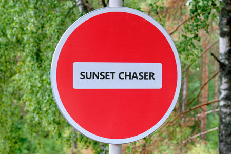 A red circle sign with a white stripe in the middle tells us that it is for sunset chasers. Trees and sky in the background.の写真素材