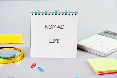 A notebook displays NOMAD LIFE on a desk alongside a calculator, sticky notes, paper clips, and a magnifier, suggesting planning for a minimal and mobile existence.の写真素材