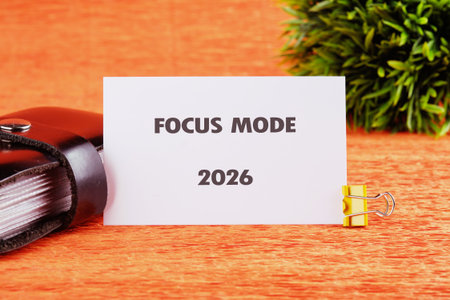 A white card stating Focus Mode and the year 2026 is displayed. The card is held up by a yellow clip and sits on an orange surface next to a black wallet and green plant.の写真素材
