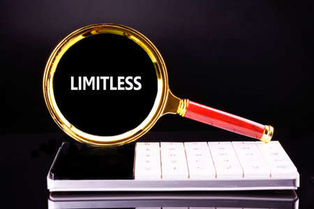 A gold magnifying glass hovers over a calculator, highlighting the word LIMITLESS within its lens, suggesting limitless possibilities and infinite potential.の写真素材