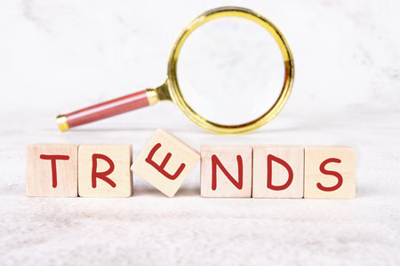 Wooden blocks spell out TRENDS with a magnifying glass above them. One block is tilted, adding a dynamic element. This setup suggests exploration and discovery.の写真素材