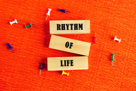 Three wooden blocks displaying the words Rhythm Of Life are presented on an orange background. Colorful push pins accent the scene, suggesting connectivity.の写真素材