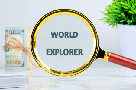 A golden magnifying glass focuses on the words WORLD EXPLORER. A small stack of tied United States currency sits to the left, and a potted green plant adds a touch of nature.の写真素材