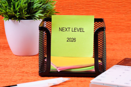 A desk shows a note saying Next Level 2026. A pot of artificial plants and office supplies sit...