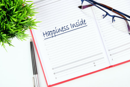 An open notebook displays the handwritten phrase Happiness Inside. Eyeglasses rest on the pages,...