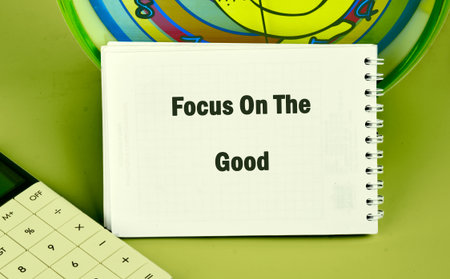 A notebook displays the phrase Focus On The Good, next to a calculator, with a Clock nearby on a...