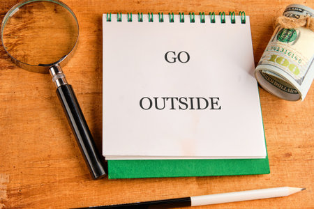 A motivational note urges a break from indoor routines, encouraging outdoor exploration. A magnifying glass, pencil, and money evoke curiosity and adventure.の写真素材
