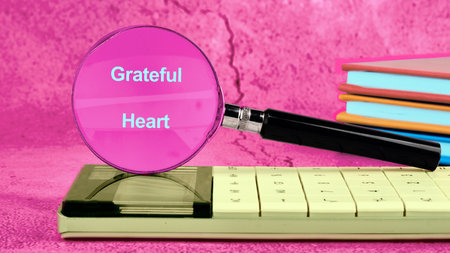 A bright scene showcases a magnifying glass highlighting the words Grateful Heart on a calculator. Colorful books stack nearby, creating a cheerful, inviting atmosphere for reflection.の写真素材