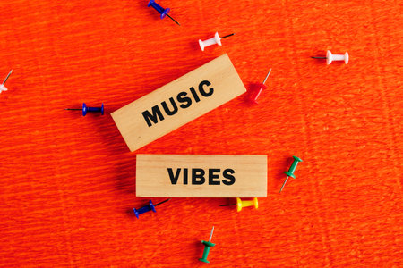 Bright orange surface showcases wooden blocks spelling music vibes surrounded by colorful push pins,...
