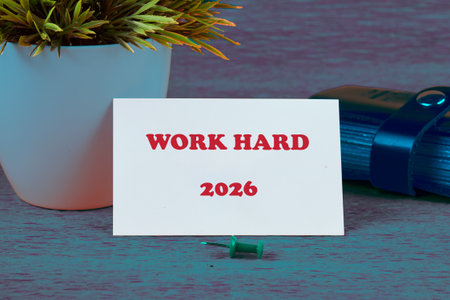 A small card saying Work Hard sits by a green pushpin and stylish notebook, surrounded by a bright...