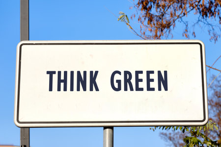 A bold sign stands prominently against a bright blue sky, encouraging passersby to embrace eco-friendly practices by thinking green. The message is clear and inspiring.の写真素材