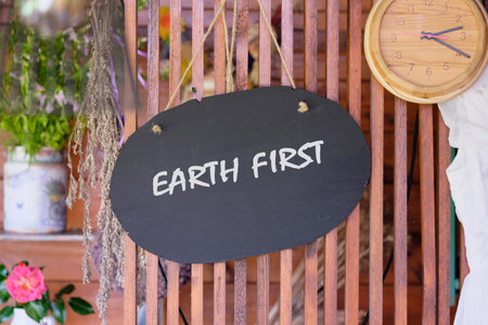 A charming wooden sign with the words Earth first hangs in a cozy rustic setting. The natural elements and warm tones encourage a message of environmental awareness and care.の写真素材