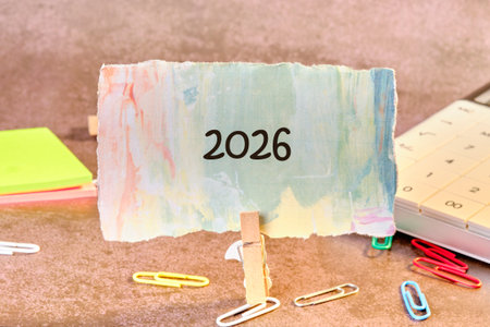 A colorful card displaying the year 2026 is held up by a clothespin against a soft, textured backdrop. Stationery items surround the scene, adding a creative touch.の写真素材