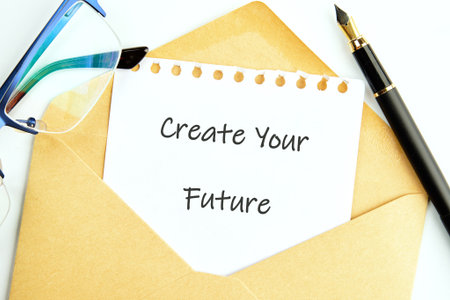 A note saying Create Your Future is placed inside a brown envelope. Beside it, there are glasses and a pen, symbolizing preparation and vision for upcoming opportunities.の写真素材