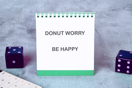 A cheerful notepad displaying the uplifting phrase Donut Worry Be Happy sits on a soft gray surface...