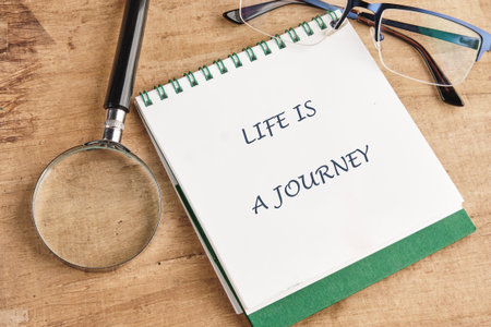 A notebook with the words Life is a journey sits beside a magnifying glass and glasses, inviting...