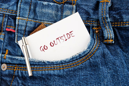 A note with the words go outside peeks from a blue denim pocket. The setting suggests a casual day, promoting adventure and the joy of exploring nature. Perfect for outdoor enthusiasts.の写真素材
