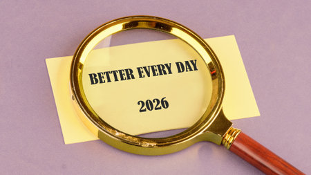 A magnifying glass hovers over a yellow note with the words better every day and the year 2026. This...