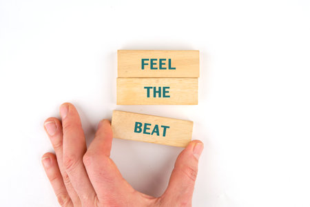A hand reaches for wooden blocks arranged to spell out feel the beat. The minimalist design highlights the tactile experience, inviting viewers to engage with rhythm and creativity.の写真素材