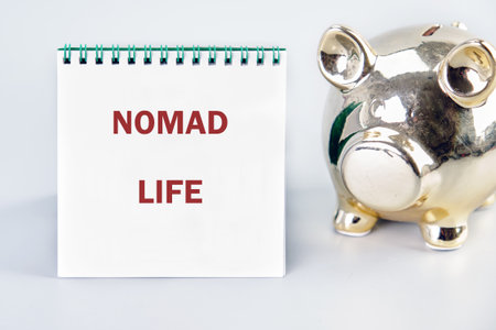 A notebook displaying the words NOMAD LIFE sits next to a shiny, golden piggy bank. It suggests saving for a lifestyle of travel and adventure.の写真素材
