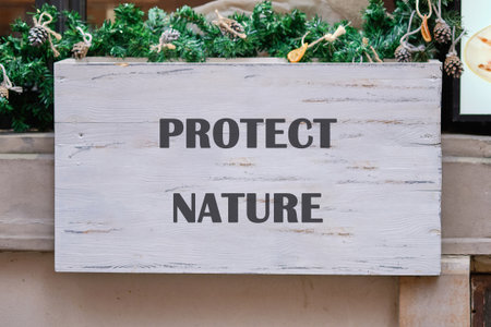 A whitewashed wooden sign reads PROTECT NATURE in dark gray letters. The sign is adorned with evergreen garland and pinecones, placed above an entrance.の写真素材