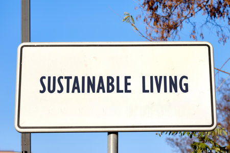 A rectangular white sign says Sustainable Living in dark blue letters, under a clear blue Autumn sky, promoting a green lifestyle near some trees.の写真素材