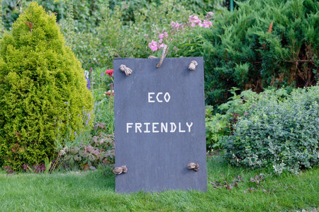 A rustic dark gray sign proclaims ECO FRIENDLY in white letters in a vibrant garden setting. Green grass and various plants create a peaceful, natural backdrop.の写真素材