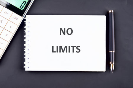 A notebook with the words NO LIMITS is on a black table with a calculator and pen, ready for work or...