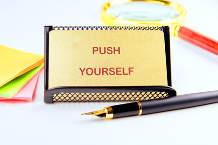 An encouraging message of PUSH YOURSELF sits in a holder with a fountain pen, notepad, and magnifying glass nearby, suggesting contemplation and forward motion.の写真素材