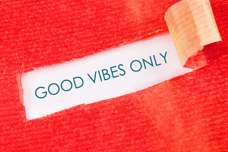 Red textured paper is torn open to reveal the message GOOD VIBES ONLY in a teal typeface. A sliver of white paper can be seen, curling at the top right corner.の写真素材