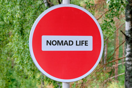 A round red and white sign with the words NOMAD LIFE is placed in a park. The sign seems to prohibit living a wandering existence in nature.の写真素材