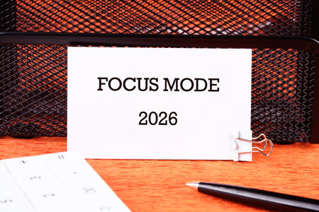 On a wooden desk, a note is clipped with FOCUS MODE 2026 printed on it. A pen and calculator are nearby, hinting at intense work ahead in the coming year.の写真素材