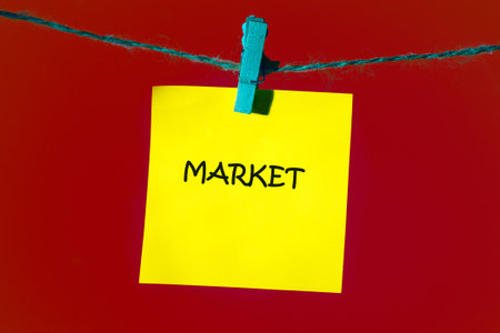 A cheerful yellow sticky note displaying the word market is clipped to a turquoise string. The vivid red background adds a pop of color, creating an inviting and lively atmosphere.の写真素材