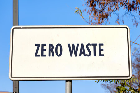 A rectangular white sign with a black border displays the words ZERO WASTE in bold, dark blue lettering under a clear blue sky with tree branches in the background.の写真素材