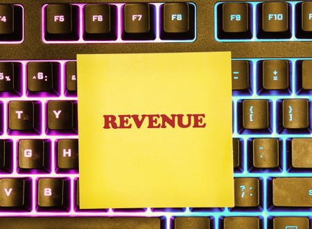 A bright yellow sticky note with the word revenue is placed on a vibrant, backlit keyboard.の写真素材