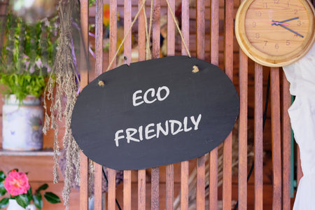 A round, dark sign proclaims Eco Friendly against a wooden backdrop. Flowers, greenery, and a clock accent the scene, suggesting a commitment to nature and timeless values.の写真素材