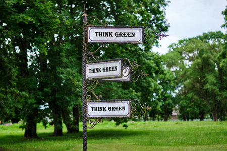 An ornate metal signpost displays three identical signs reading THINK GREEN. They stand in a green...