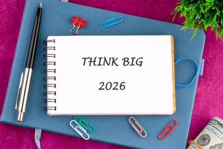A vibrant notebook lays on a pink surface, featuring the words THINK BIG with the year 2026....