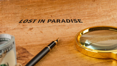 A wooden table displays a pen, magnifying glass, and cash, symbolizing adventure and exploration in a paradise setting. The words lost in paradise invite curiosity and wonder.の写真素材