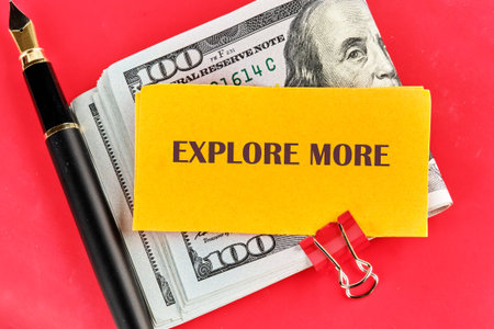A stack of hundred-dollar bills lies under a bright yellow note encouraging exploration. A sleek pen rests nearby, inviting creativity and ambitious plans for new ventures.の写真素材