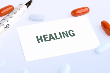 A collection of colorful tablets, a syringe, and a card displaying the word healing, all arranged neatly to symbolize recovery and health in a serene setting.の写真素材