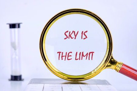 A magnifying glass focuses on the words sky is the limit, symbolizing ambition and potential. In the background, an hourglass rests, representing the value of time in achieving goals.の写真素材
